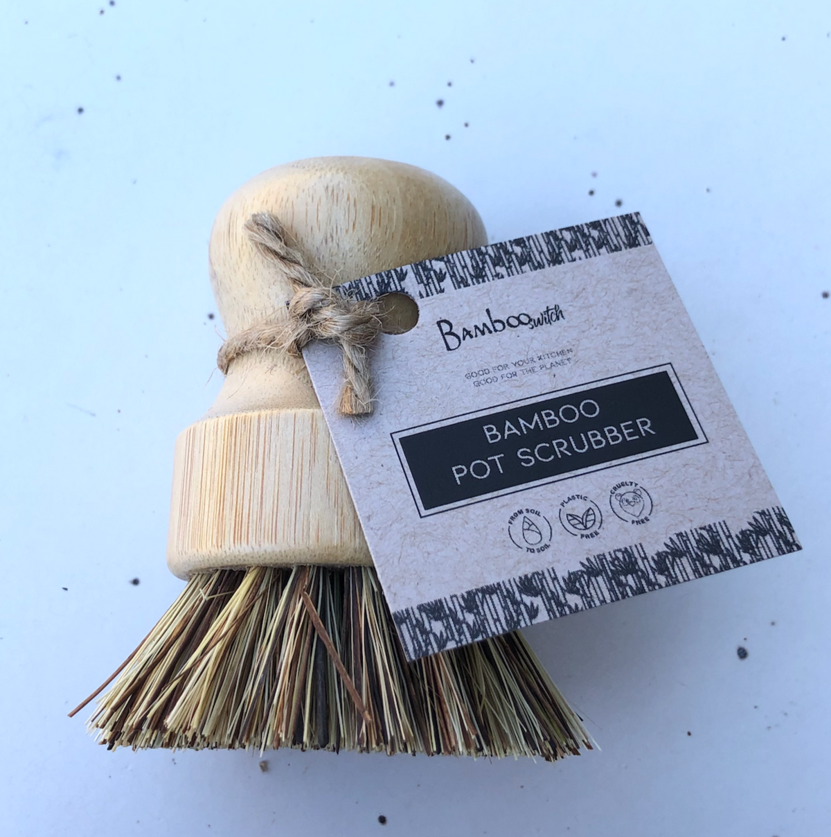 A bamboo pot scrubber with tough bristles, tied with a string to a branded card that reads 'Bamboo Pot Scrubber'.