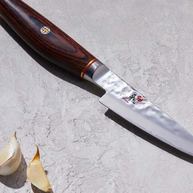 Close up of Miyabi Artisan Paring knife on textured white background.