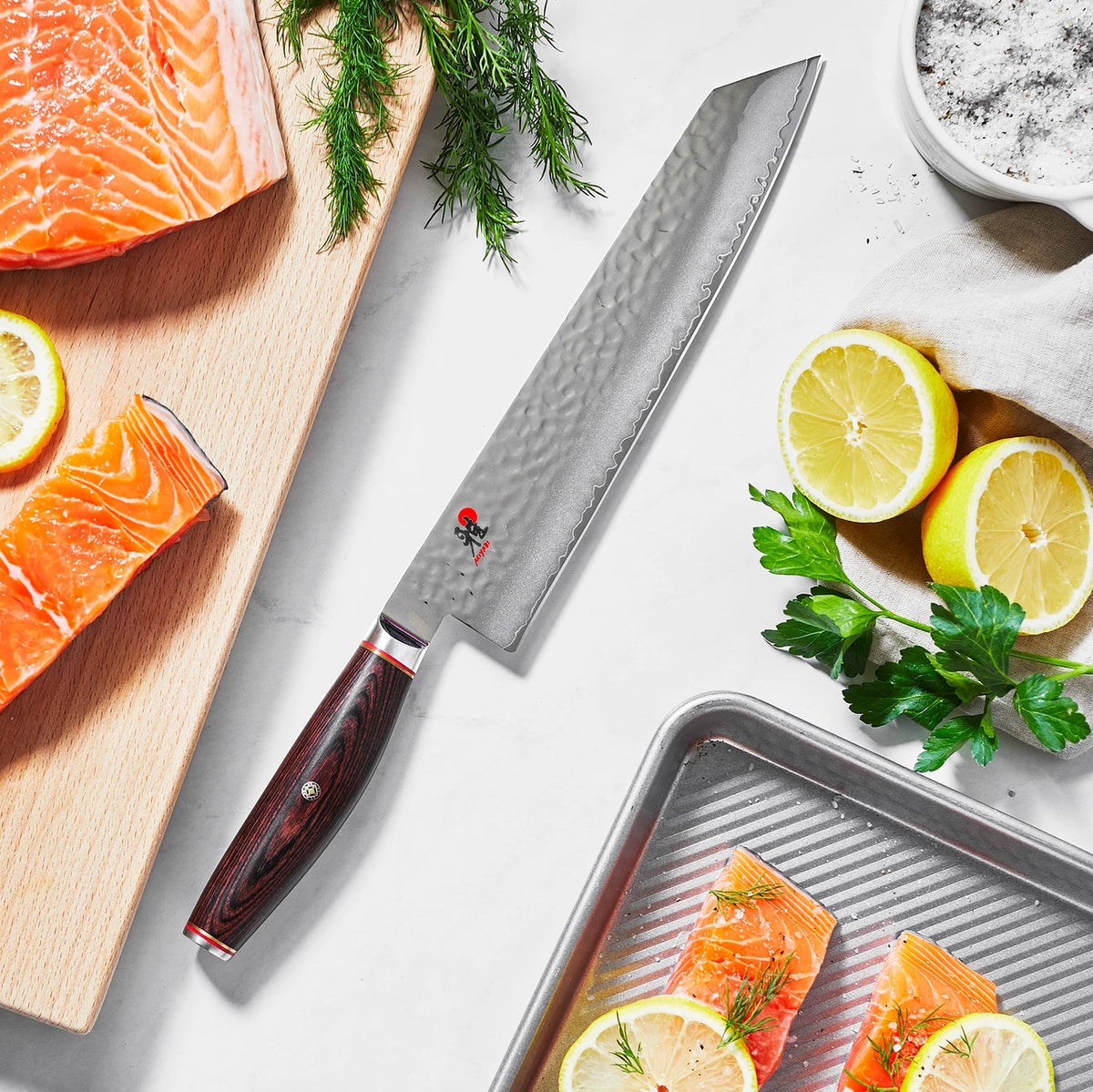 Miyabi Artisan Kiritsuke on white background with salmon, lemons, dill and salt.