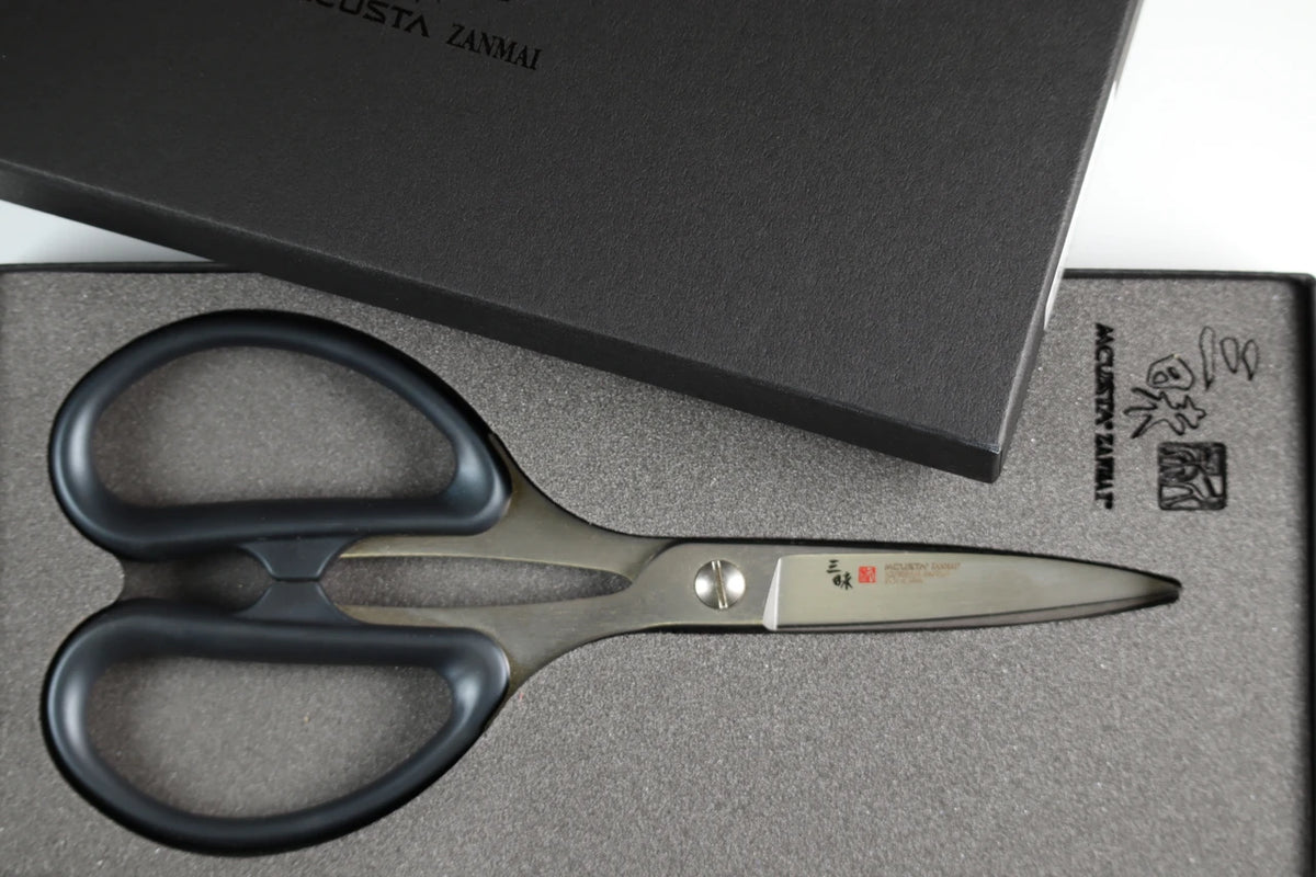 Pair of black-handled scissors on a gray surface with a black box in the background.