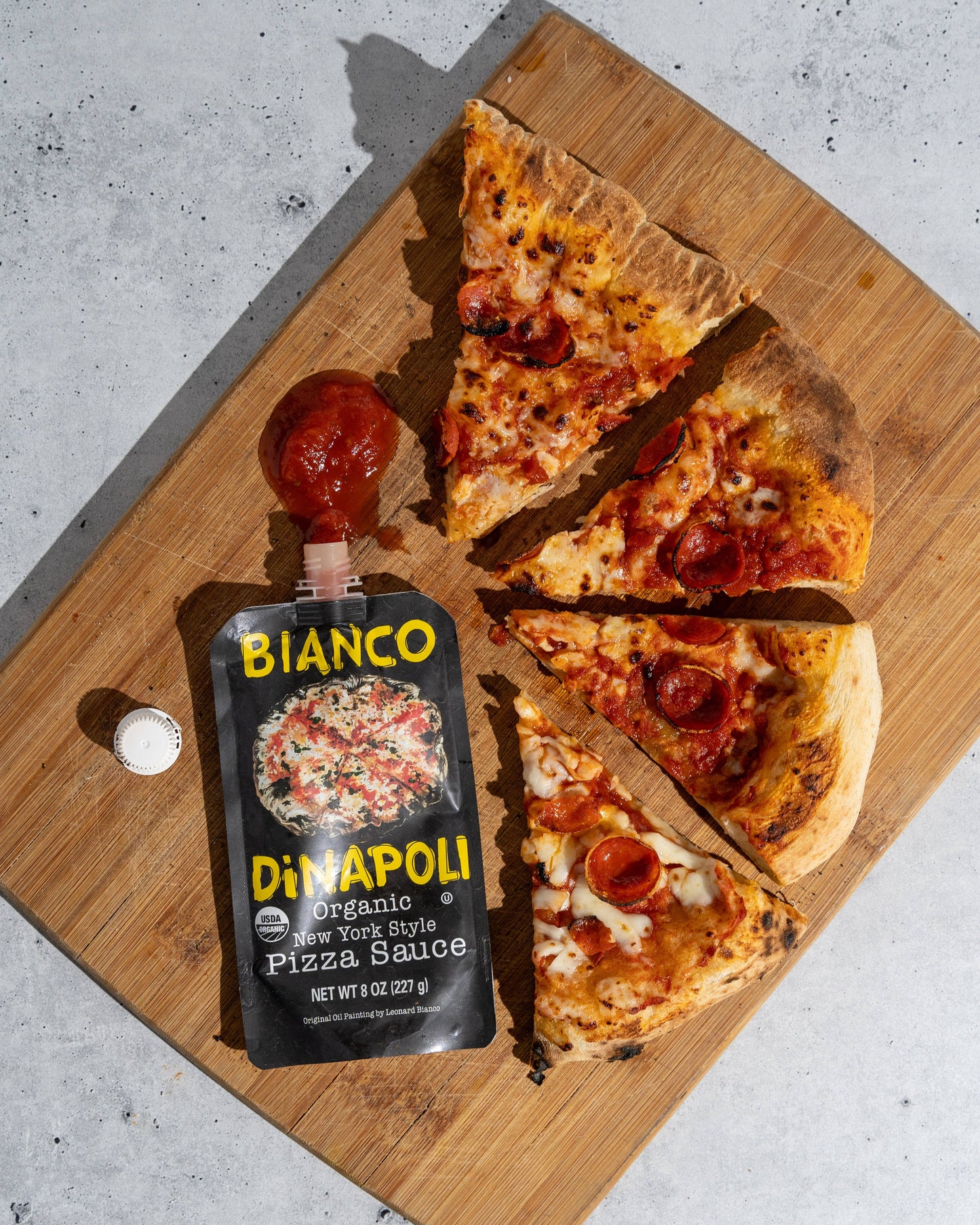 Slices of pizza on a wooden board with a pouch of Bianco pizza sauce.