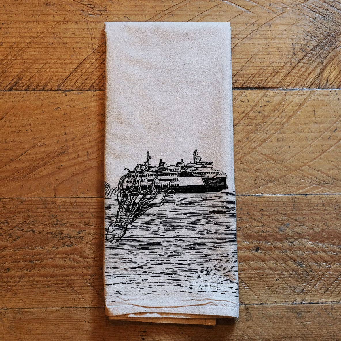 Folded towel with a ferry entangled with a kraken on a wooden surface
