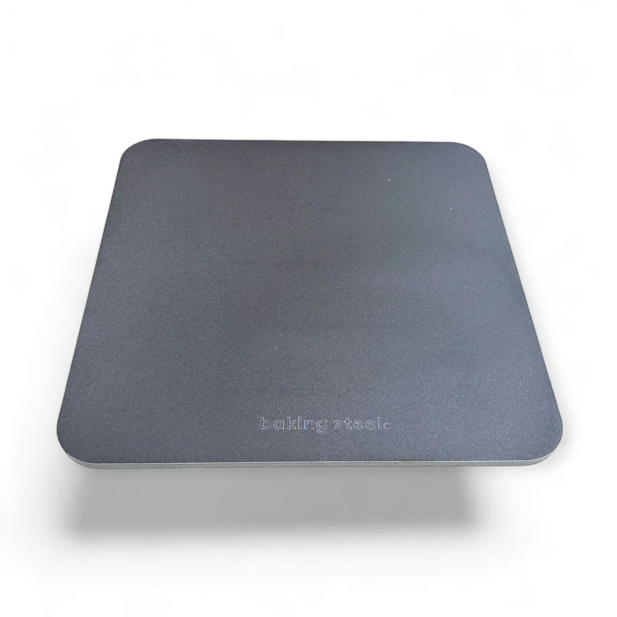 A square dark gray carbon baking steel with rounded corners and the brand name 'baking steel' printed in light gray near the bottom center, shown on a white background with a soft drop shadow.