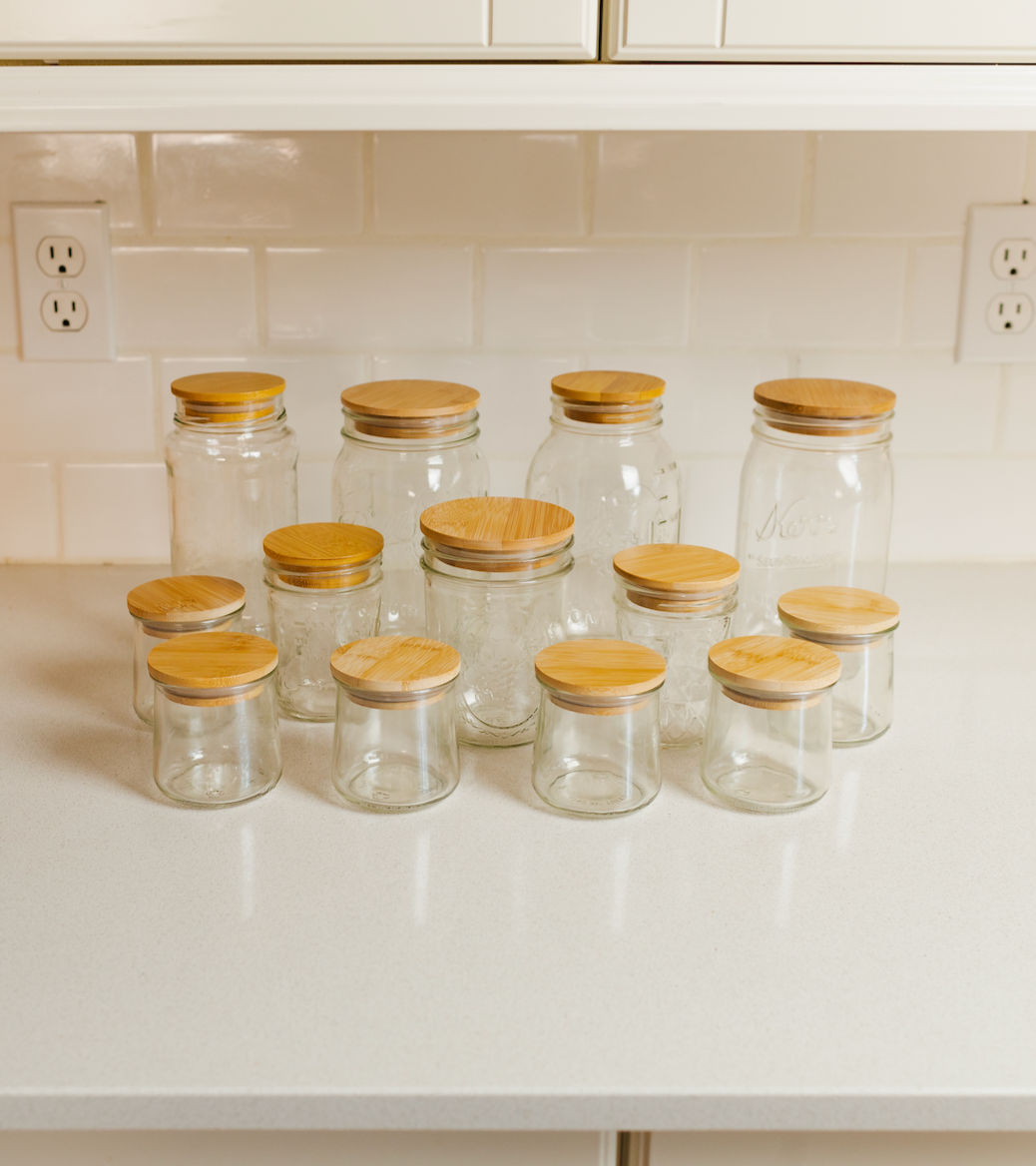 A collection of glass jars with reusable bamboo jar lids on a kitchen counter.