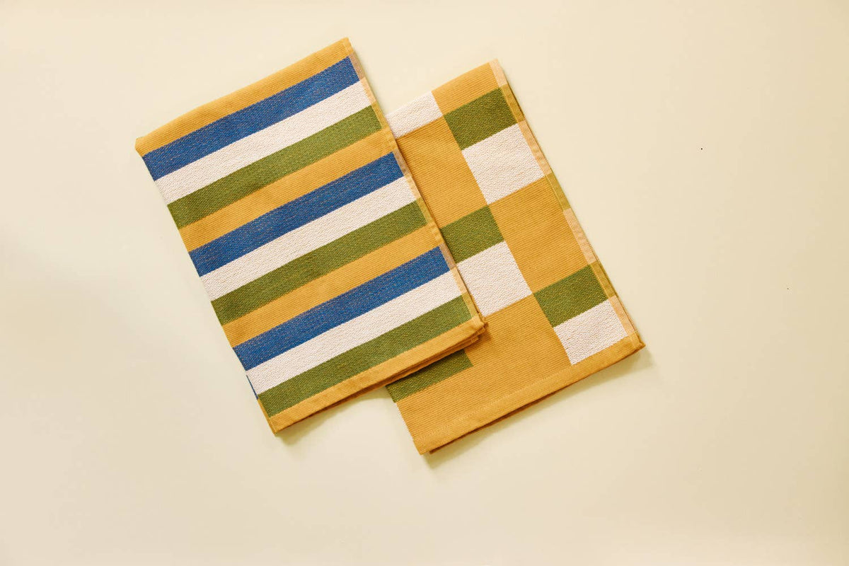 Two folded striped fabric napkins in yellow, blue, green, and white, arranged on a light cream background.