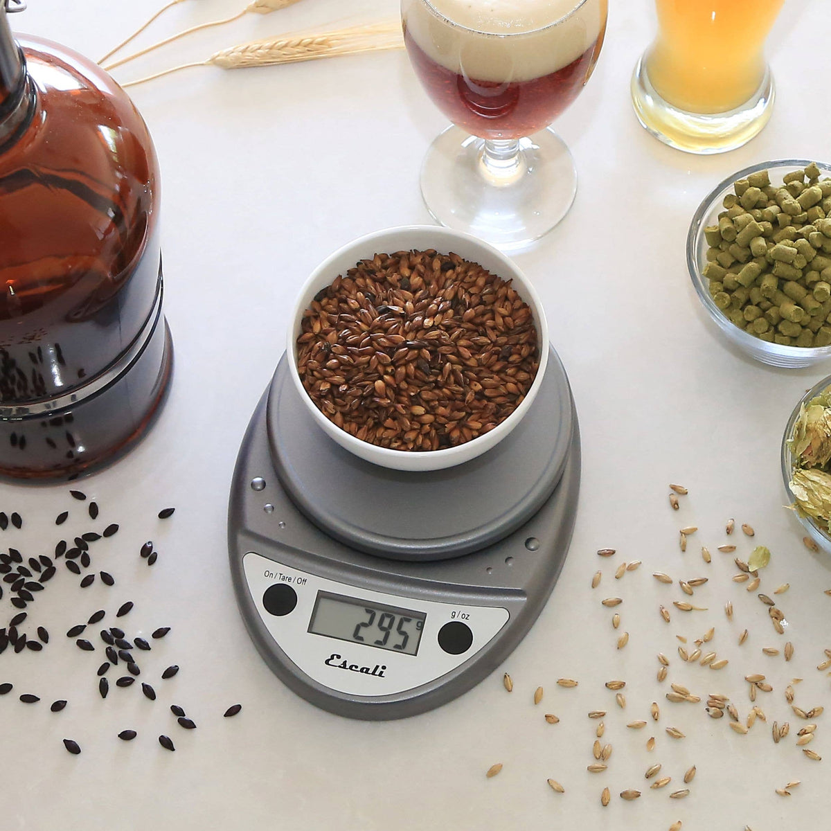 Digital kitchen scale with a bowl of seeds on a table with various seeds and a glass of beer.