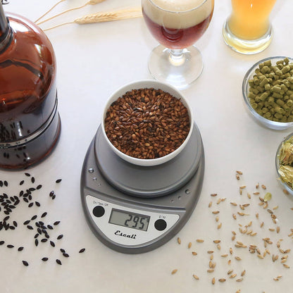 Digital kitchen scale with a bowl of seeds on a table with various seeds and a glass of beer.