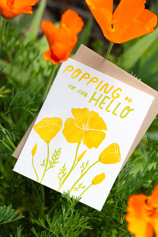 Greeting card with yellow flowers and 'Popping to say Hello' text, surrounded by orange flowers.