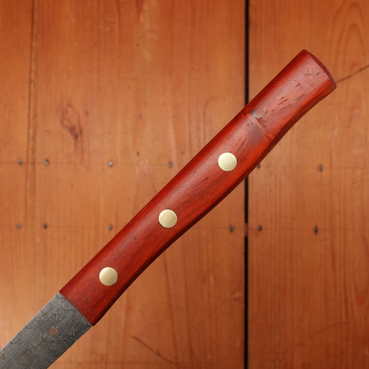 Wooden-handled knife with three metal rivets against a wooden background