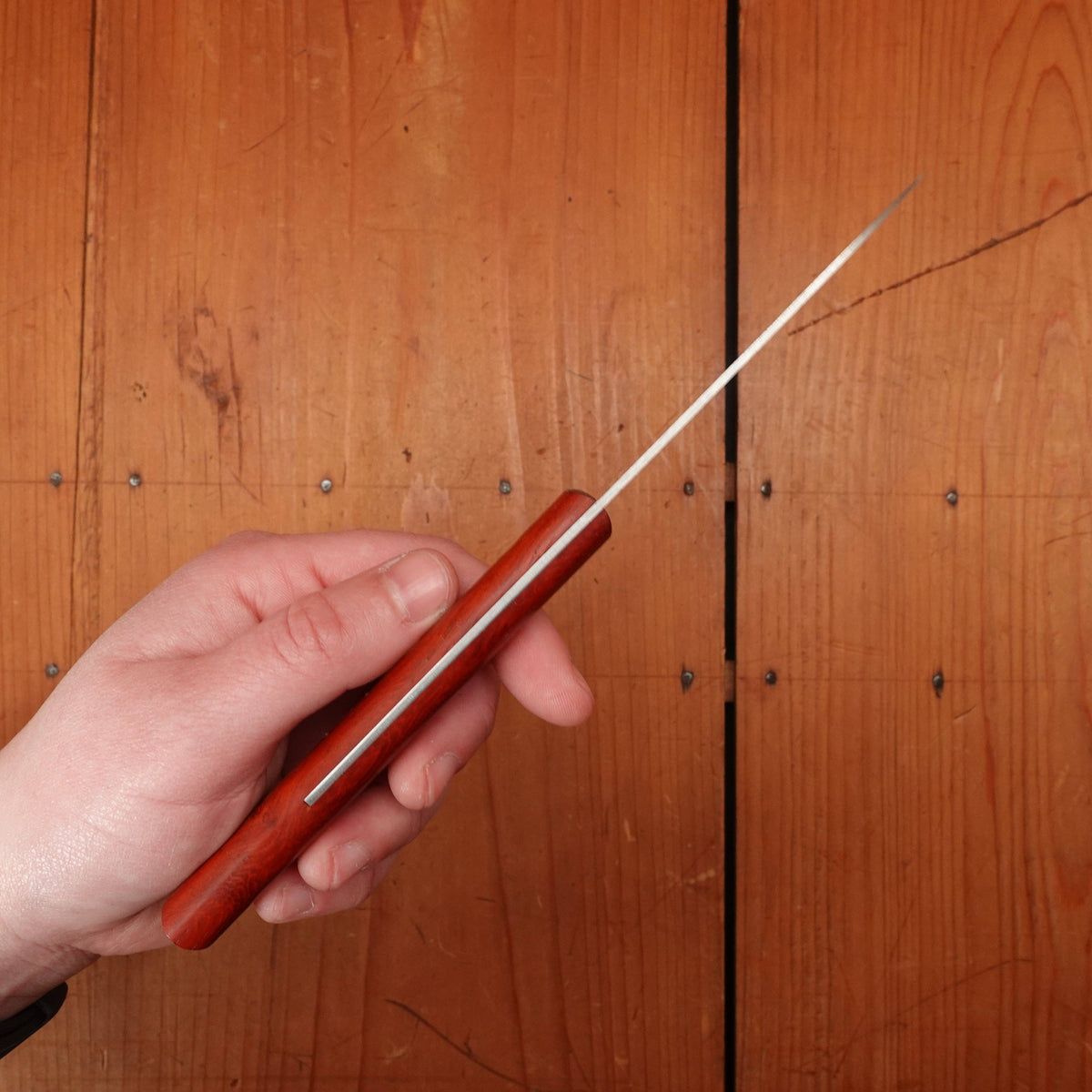 Hand holding a red-handed knife against a wooden background
