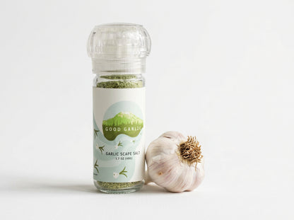 A bottle of Good Garlic Garlic Scape Salt with a clear cap and a white label, shown next to a whole garlic bulb on a clean white background.