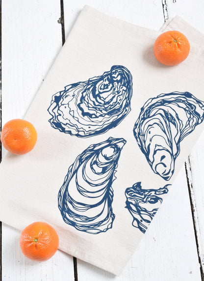 Tea towel with blue oyster print on white wood background with oranges.