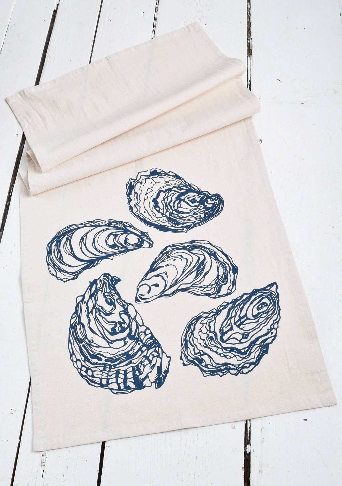 White tea towel with blue oyster prints on white wood.