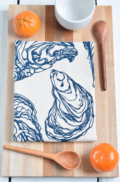 Oyster print towel on a cutting board with oranges wooden spoons and a cup.