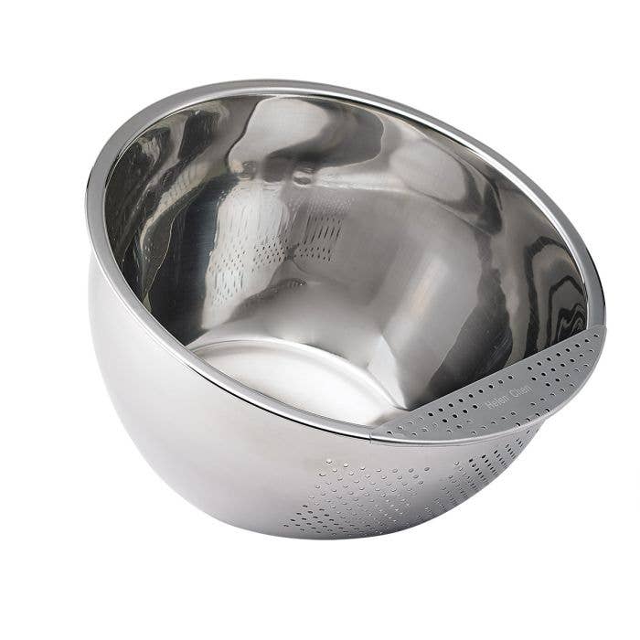 Stainless steel rice washing bowl with  perforated exterior on a white background