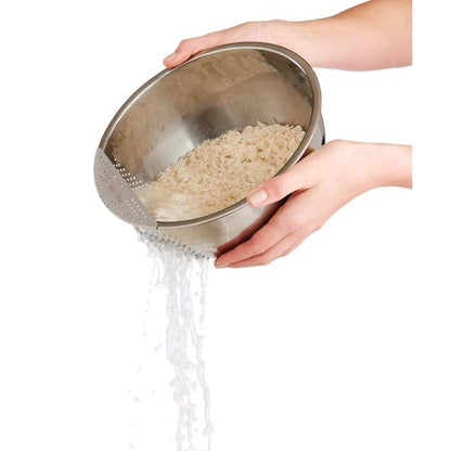 Person rinsing rice in a metal strainer over a bowl on a white background