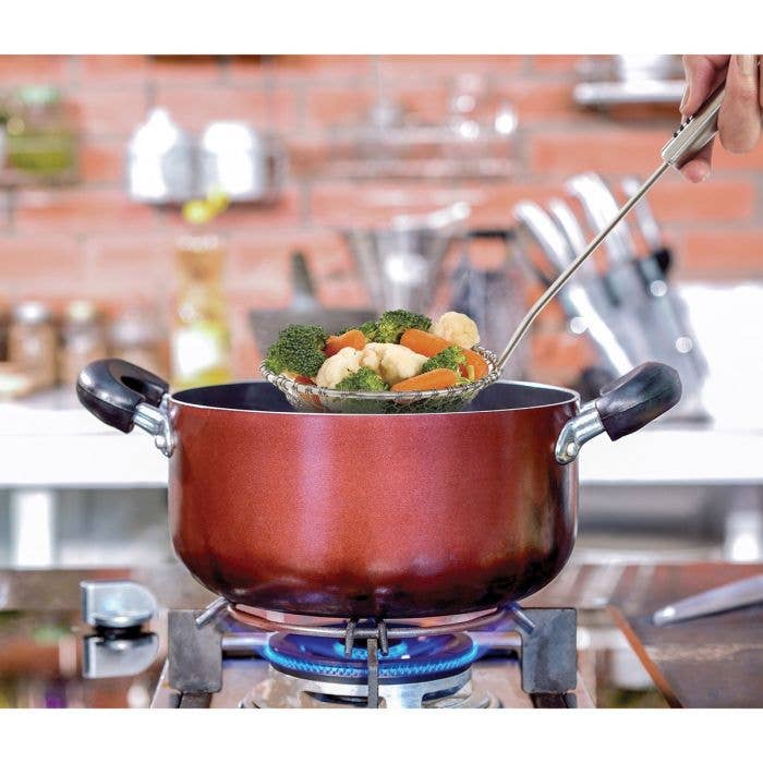 Red pot on a stove with vegetables being strained, kitchen setting