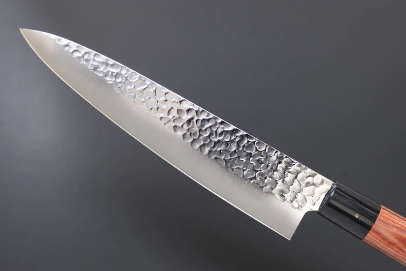 Hammered steel gyuto knife blade on a dark background