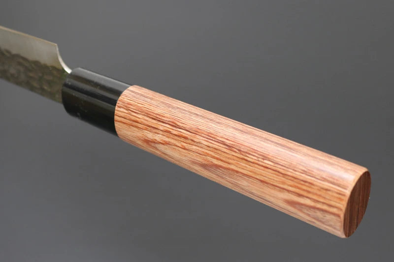 A close-up of a Japanese-style kitchen knife with a hammered steel blade and a light brown wood handle, shown against a dark gray background.