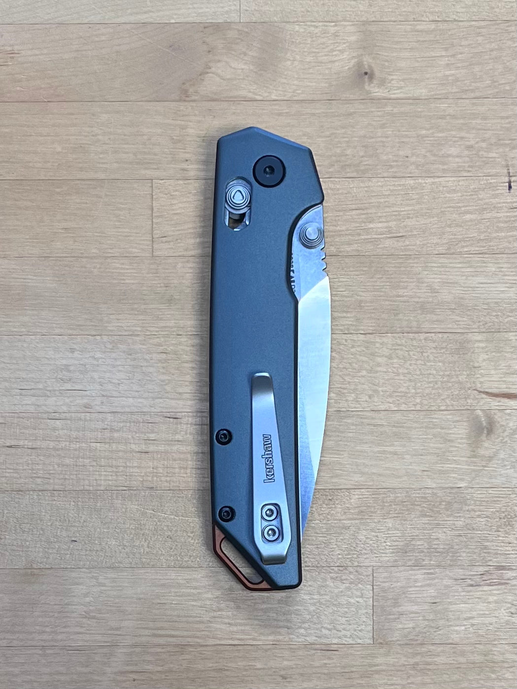 A Kershaw Iridium folding knife with a black anodized aluminum handle and a black-oxide finished blade, viewed from the closed position on a wooden surface.