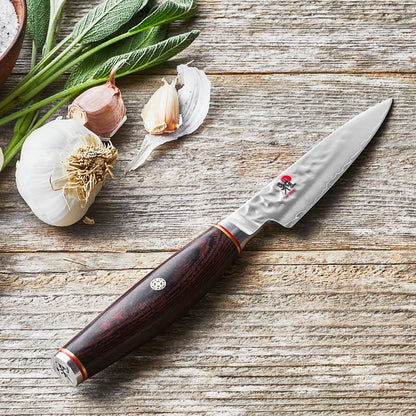 Miyabi Paring Knife on worn wood with sage and garlic.