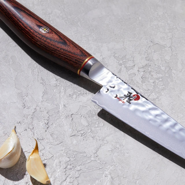 Close up of Miyabi logo on knife n a textured white background with cloves of garlic