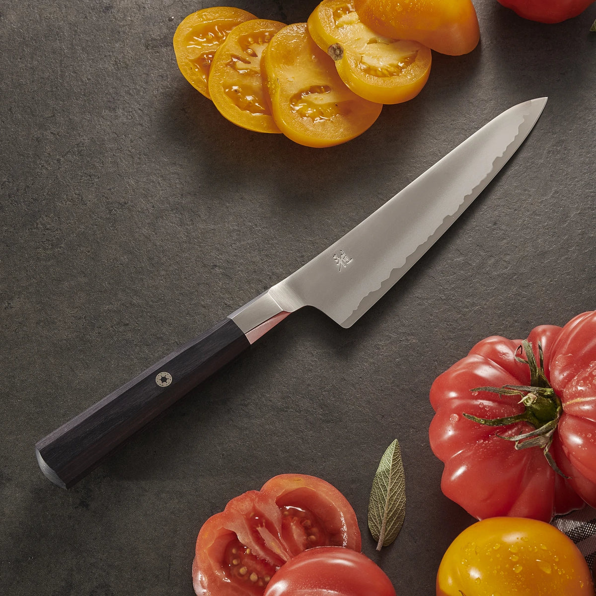 Miyabi Koh Petty knife on black textured background with heirloom tomatoes.
