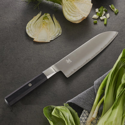 Myabi Koh Santoku on textured black background with various vegetables..