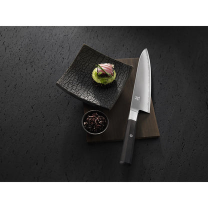 Miyabi chef knife with sushi on textured black background.