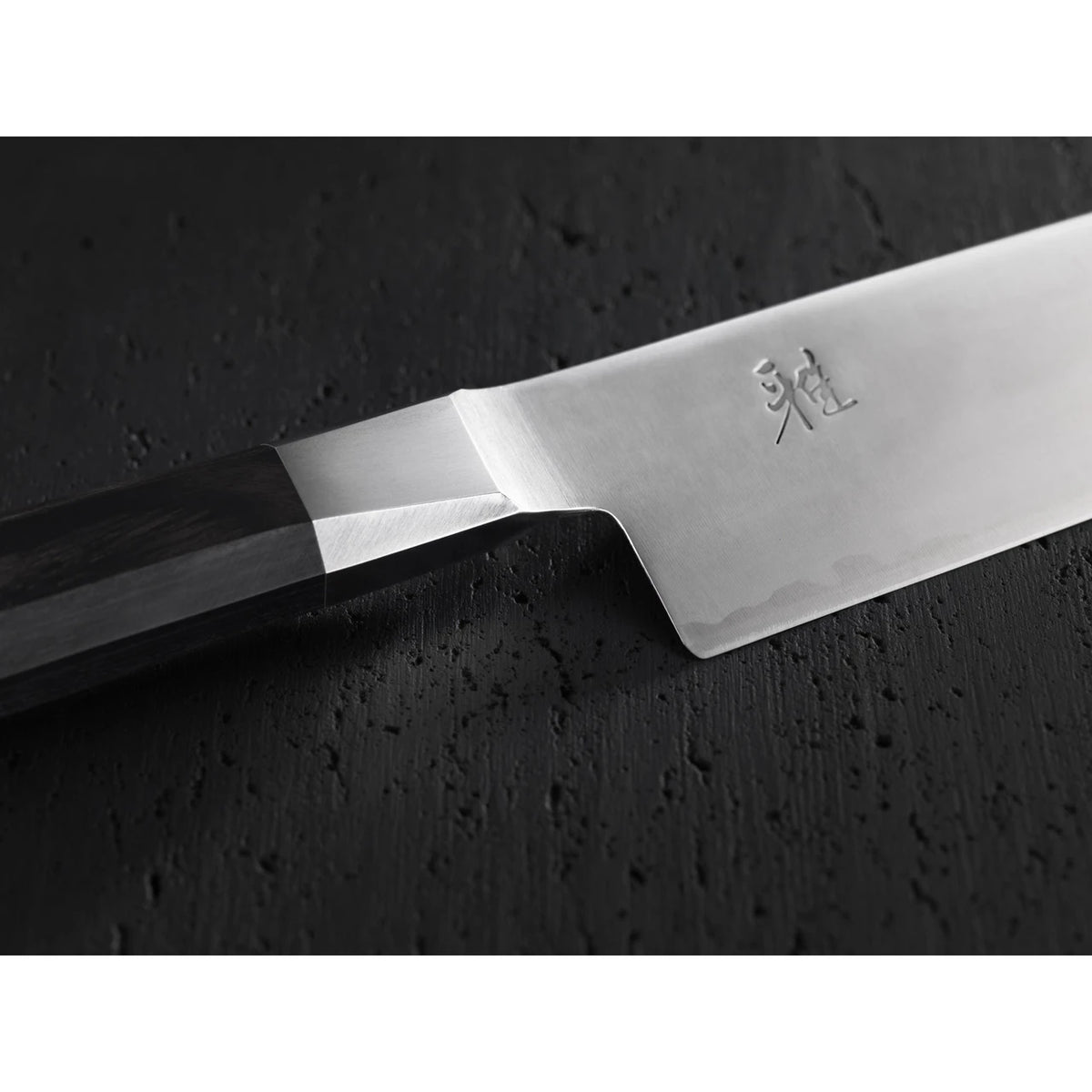 Close up of bolster, Handle-, and heel of a chef knife on a textured black background.