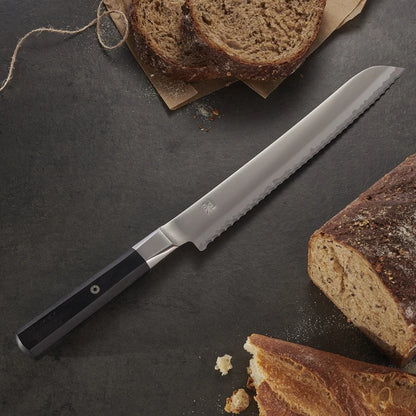 Miyabi Koh Bread knife on textured black background with bread.