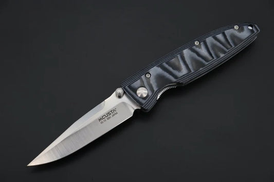 A folding pocket knife with a satin-finished silver blade and a textured blue/grey handle, shown open against a dark gray background. The blade is engraved with the brand name 'MCUSTA'