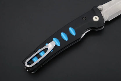 A close-up of a folding pocket knife with a black handle, bright blue accent inserts, and a silver clip, shown on a dark gray background.