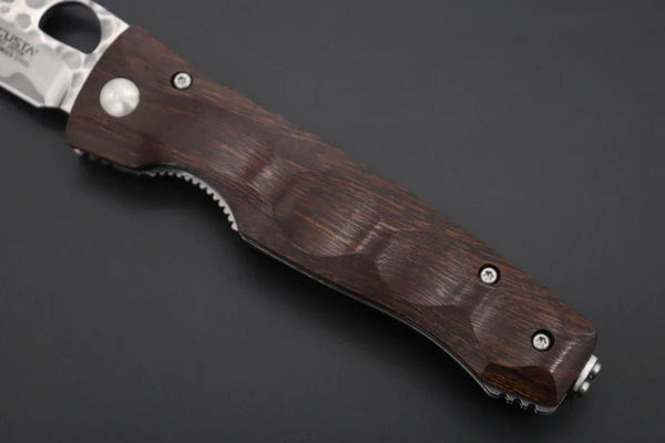 A close-up of a folding pocket knife with a dark brown wood-grain handle and a partially visible silver blade, set against a dark gray background.