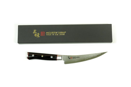 A Mcusta boning knife with a black handle and patterned steel blade, displayed below its black presentation box with gold lettering on a white background.