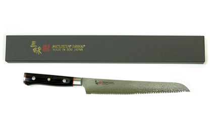 A Japanese-style kitchen knife with a patterned steel blade and black handle, displayed horizontally below its dark gray rectangular presentation box on a white background.