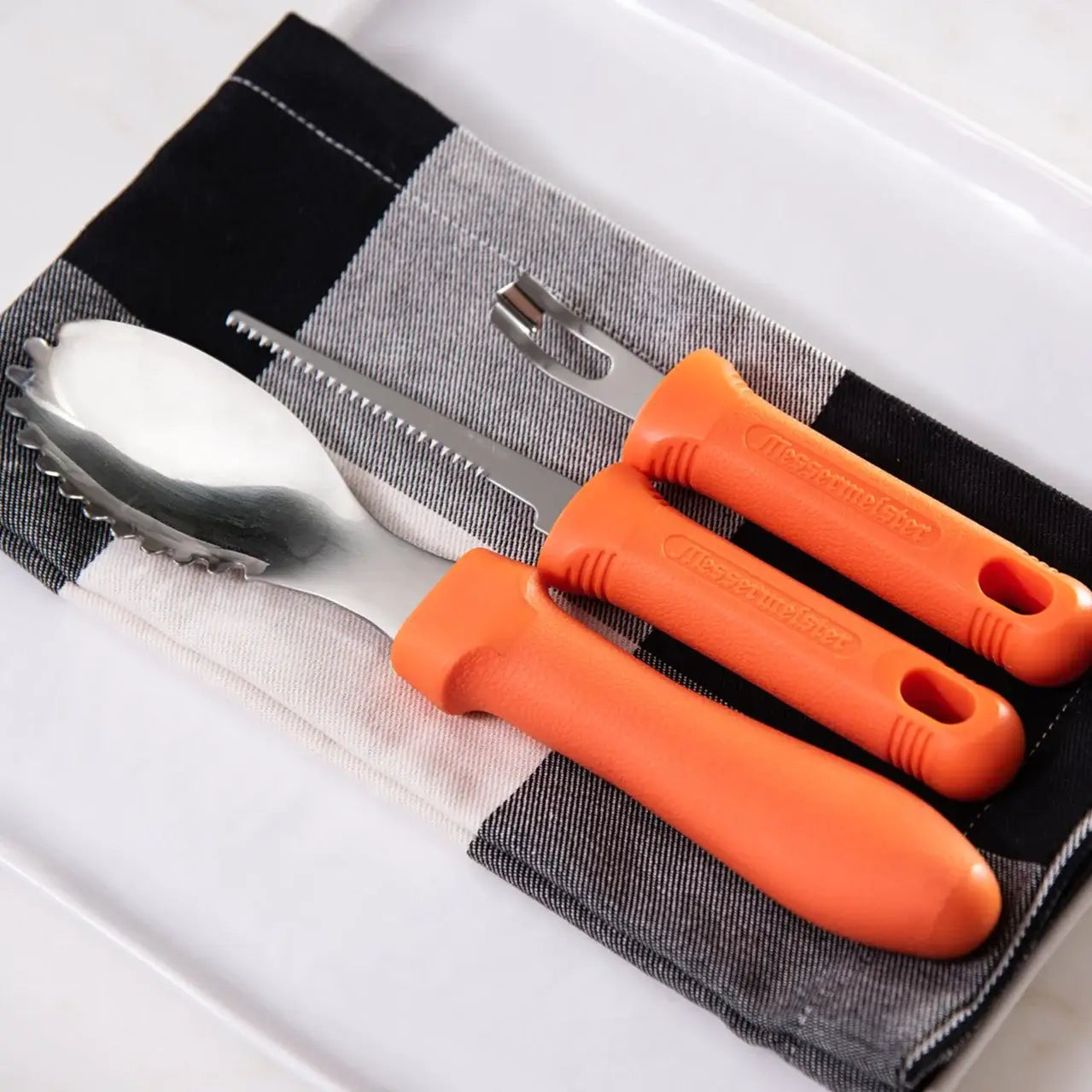 Set of orange-handled pumpkin carving utensils on a checkered cloth