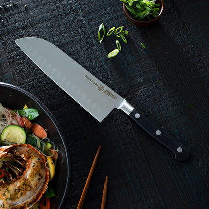 Santoku knife on a dark surface with a bowl of salad and green onions.