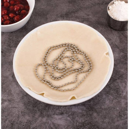 Round piece of dough with a spiral of Mrs. Anderson's Baking Pie Weight Chain, 6ft -  a gray surface, with bowls of red berries and flour in the background.
