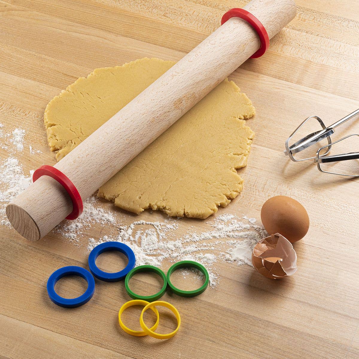 Rolling pin, cookie dough, and cookie cutters on a wooden surface with flour.