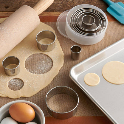 Baking tools including a rolling pin, cookie cutters, and a baking tray on a wooden surface.