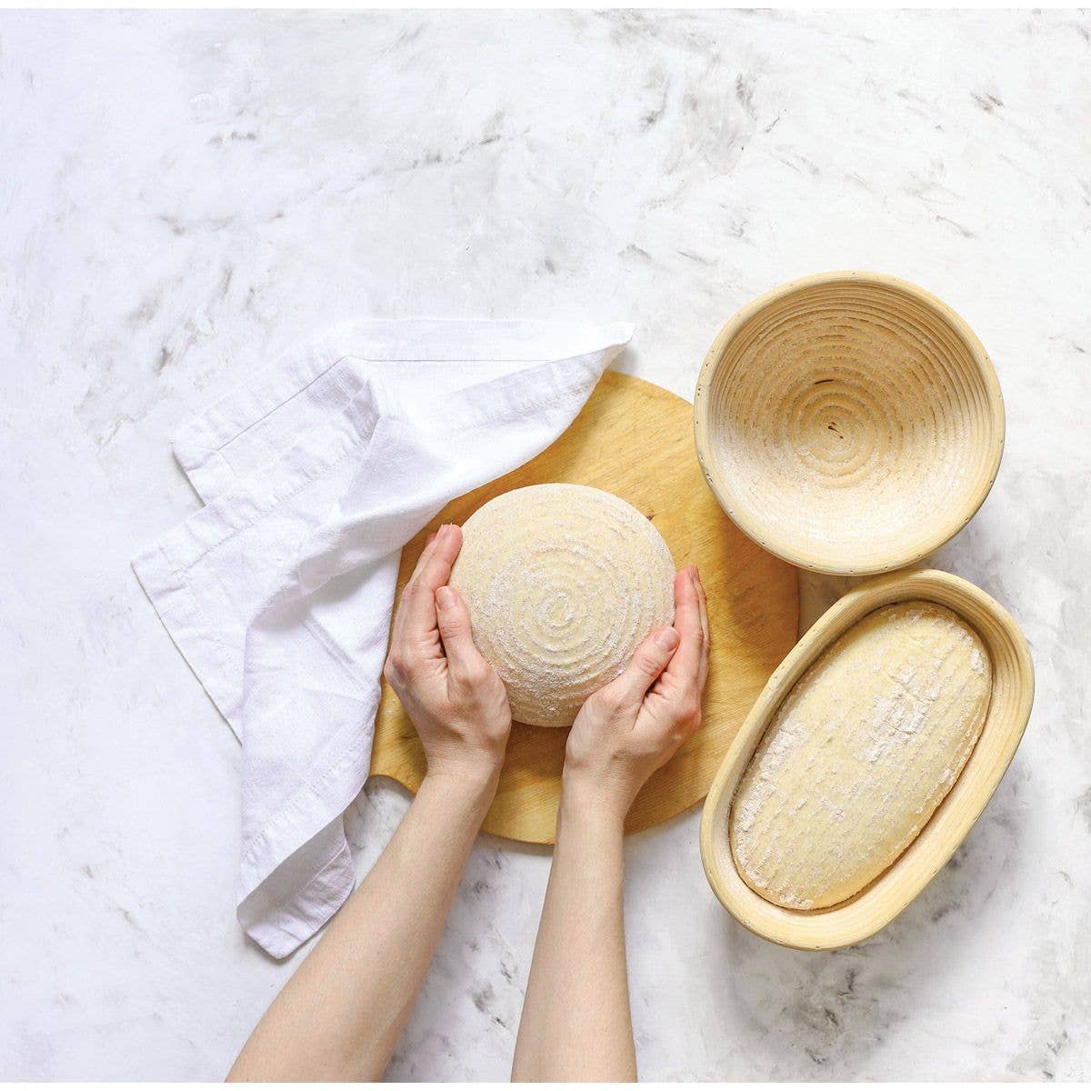 Hands holding a round bread loaf next to two other bread loaves on a marble surface.