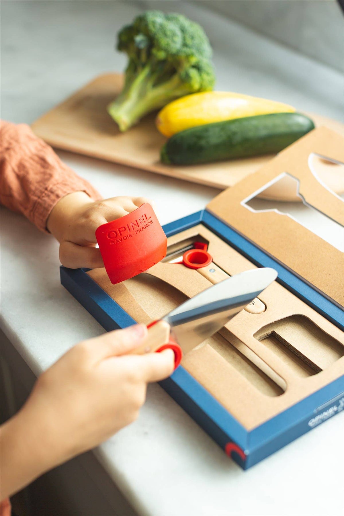 Child using Opinel le petit Chef knife set on a table with vegetables in the background