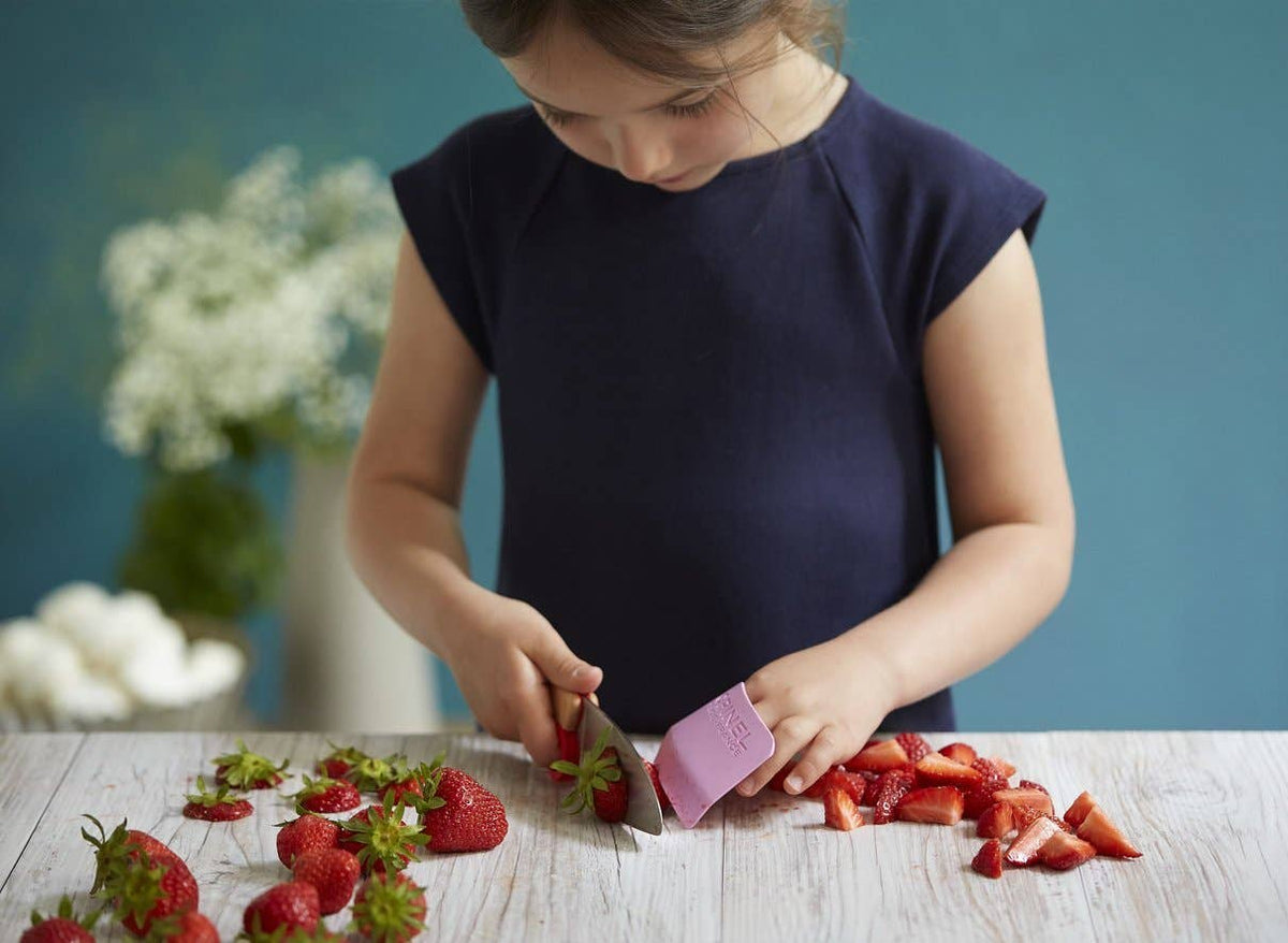 Child cutting strawberries on a wooden table with a blue background
