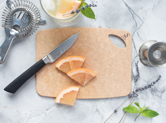 Sage cutting board with sliced grapefruit, knife, and cocktail ingredients on a marble surface