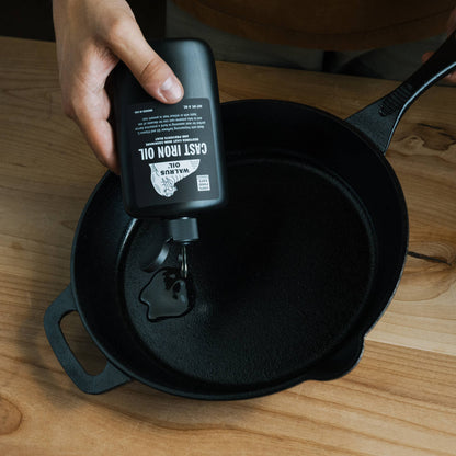 Person applying Cast Iron Oil to a black cast iron skillet on a wooden surface