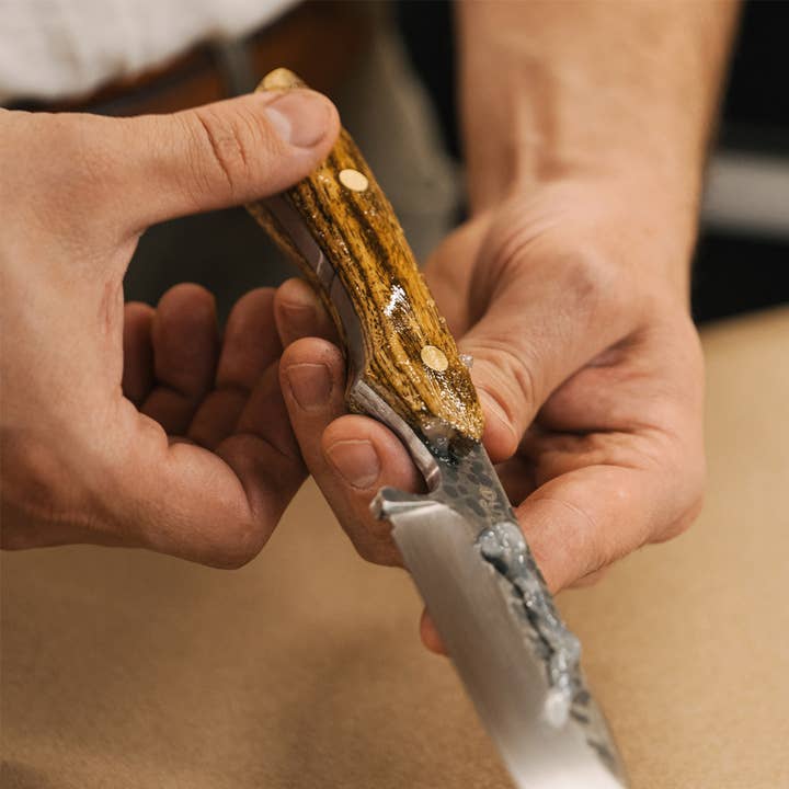 Close-up of hands holding a pocket knife with a wooden handle, with knife Oil being applied.